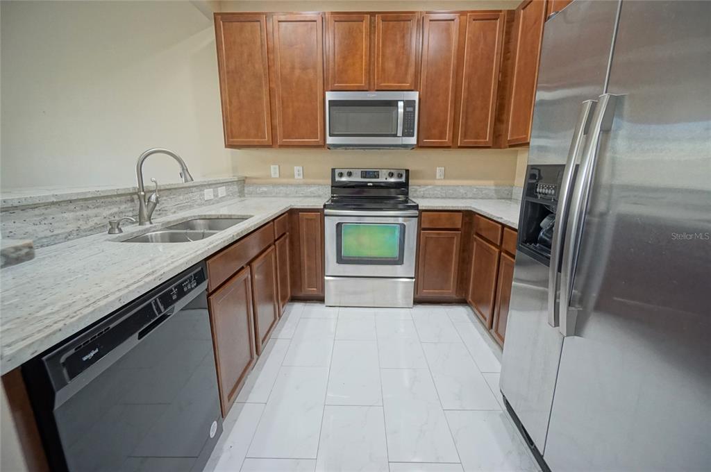 A kitchen features stainless steel appliances, wood cabinets, and light-colored granite countertops — 6888 46TH LANE N, PINELLAS PARK, FL