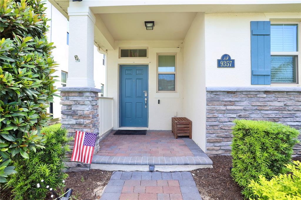 A front porch with a blue door, stone accents, and a small American flag — 9357 JAYWOOD ROAD, WINTER GARDEN, FL