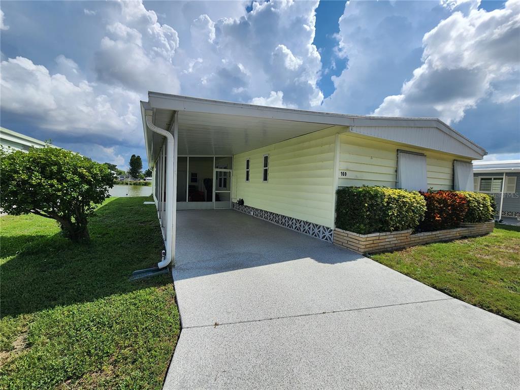 A light yellow mobile home features a concrete driveway, a carport, and a screened-in porch — 808 53RD AVENUE E UNIT 169, BRADENTON, FL