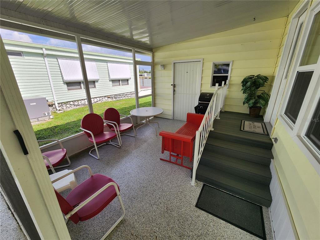 A screened-in porch features a concrete floor, red metal chairs, a bench, and stairs — 808 53RD AVENUE E UNIT 169, BRADENTON, FL