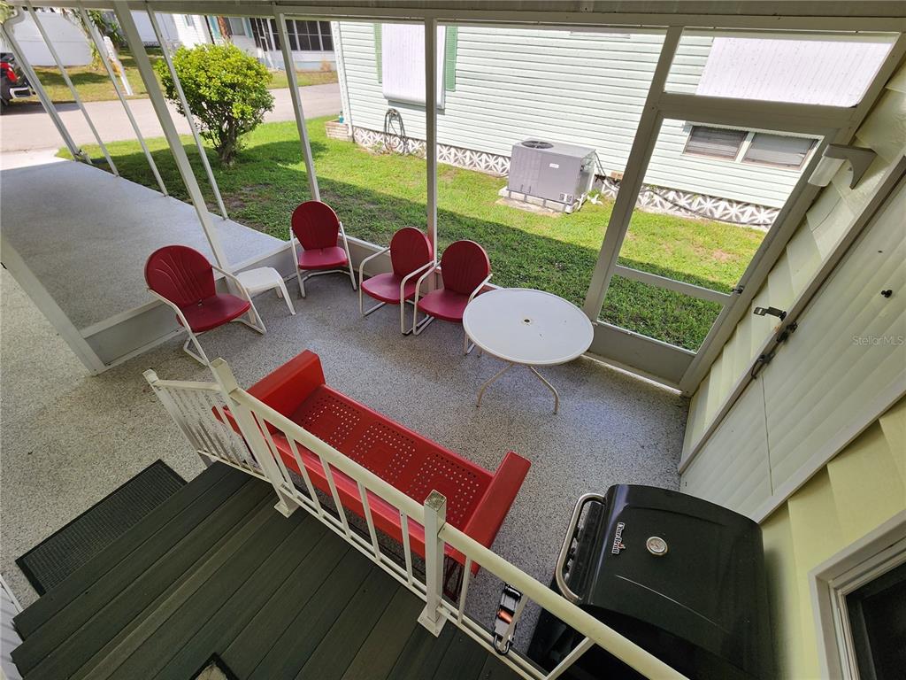 A screened-in porch features a red metal bench, four red chairs, a table, and a grill — 808 53RD AVENUE E UNIT 169, BRADENTON, FL
