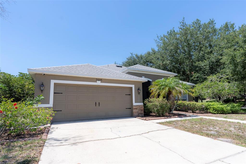 A single-story house with a tan stucco exterior, a gray shingled roof, and a garage — 7605 NOTTINGHILL SKY DRIVE, APOLLO BEACH, FL