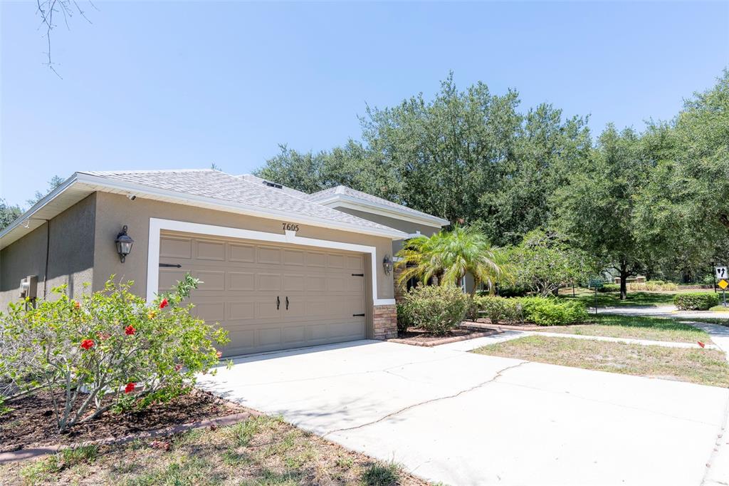 A tan house with a two-car garage and a concrete driveway under a blue sky — 7605 NOTTINGHILL SKY DRIVE, APOLLO BEACH, FL
