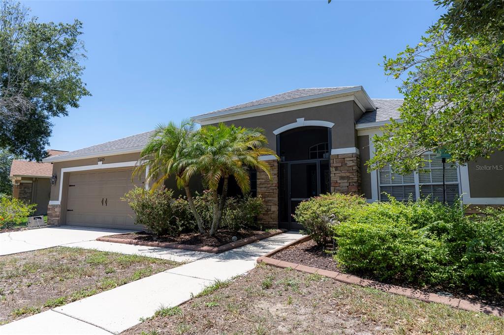 A single-story house with a two-car garage, stone accents, and a palm tree in front — 7605 NOTTINGHILL SKY DRIVE, APOLLO BEACH, FL