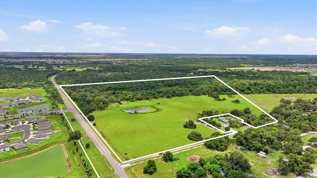An aerial view shows a large, fenced grassy lot with a pond and a house — 13805 COUNTY ROAD 675, PARRISH, FL
