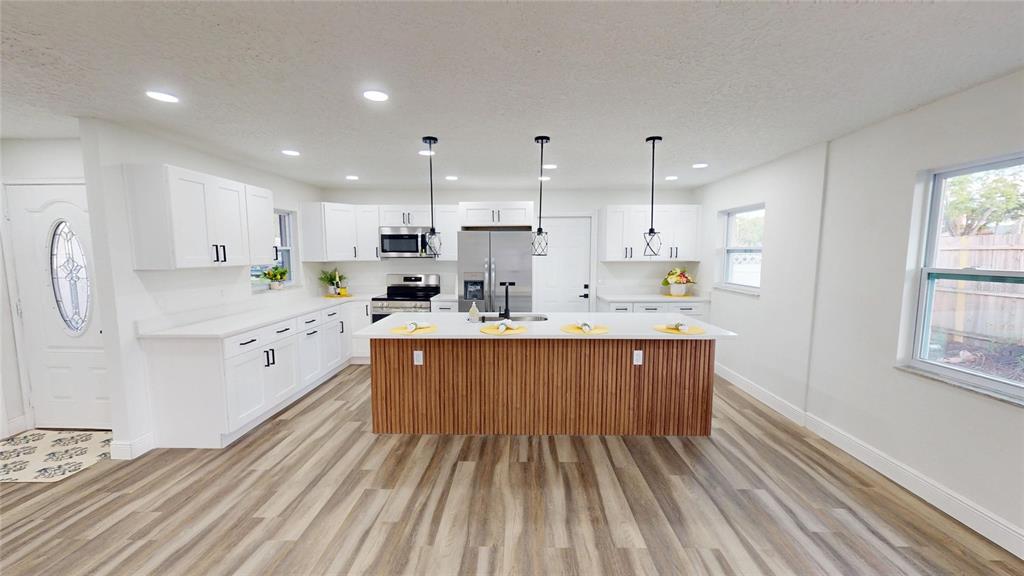 A modern kitchen features white cabinets, a wood-slatted island, and light-colored wood-look flooring — 501 HERITAGE BOULEVARD, WINTER PARK, FL