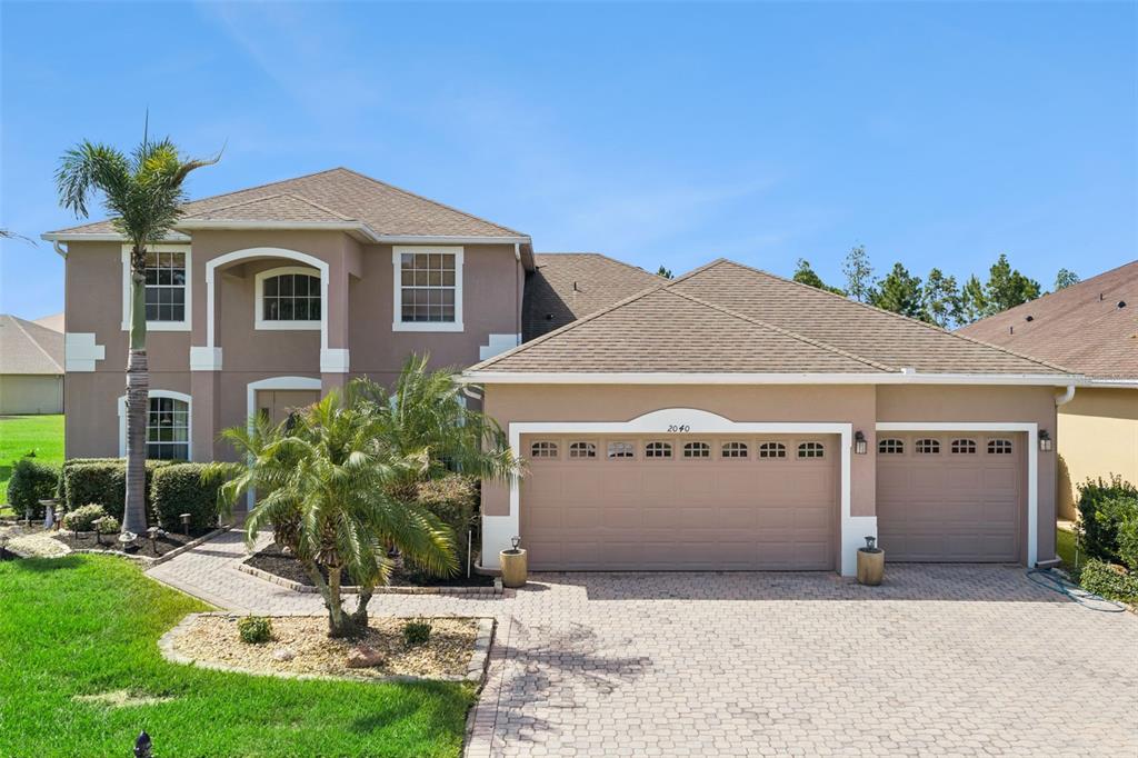 A two-story suburban house with a tan stucco exterior, a three-car garage, and a palm tree — 2040 HAWKS LANDING DRIVE, ORLANDO, FL