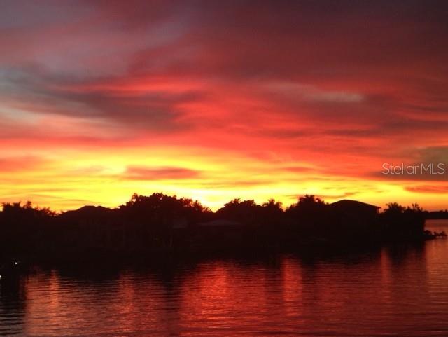 A vibrant sunset glows over a dark silhouette of trees and houses along a waterfront — 1444 HARBOR DRIVE, SARASOTA, FL