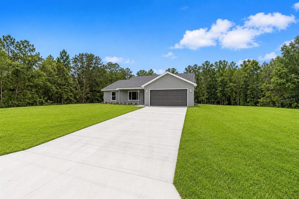 A gray single-story house with a two-car garage sits on a large, grassy lot — 19788 SW FLAMINGO DRIVE, DUNNELLON, FL