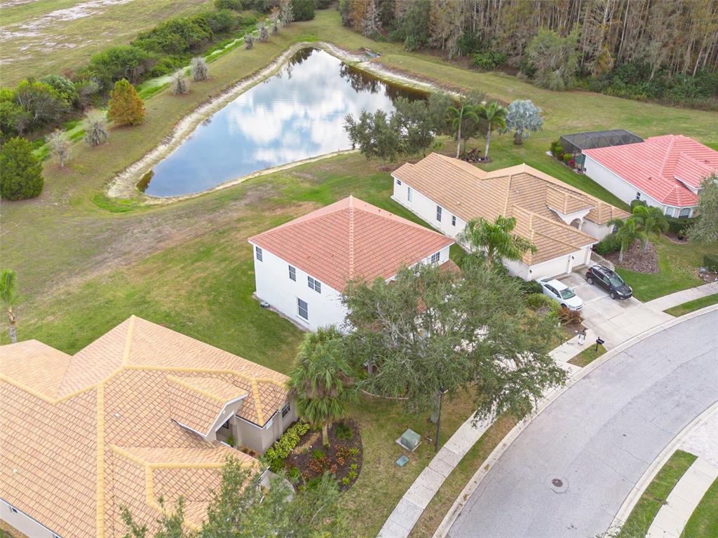 An aerial view shows suburban houses with tiled roofs near a pond and trees — 9028 WILLOWBROOK CIRCLE, BRADENTON, FL