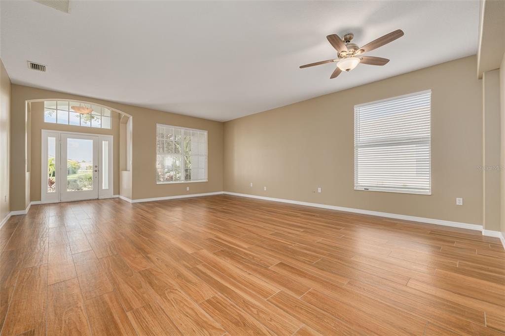 An empty living room features wood-look tile flooring, beige walls, and a ceiling fan — 9028 WILLOWBROOK CIRCLE, BRADENTON, FL