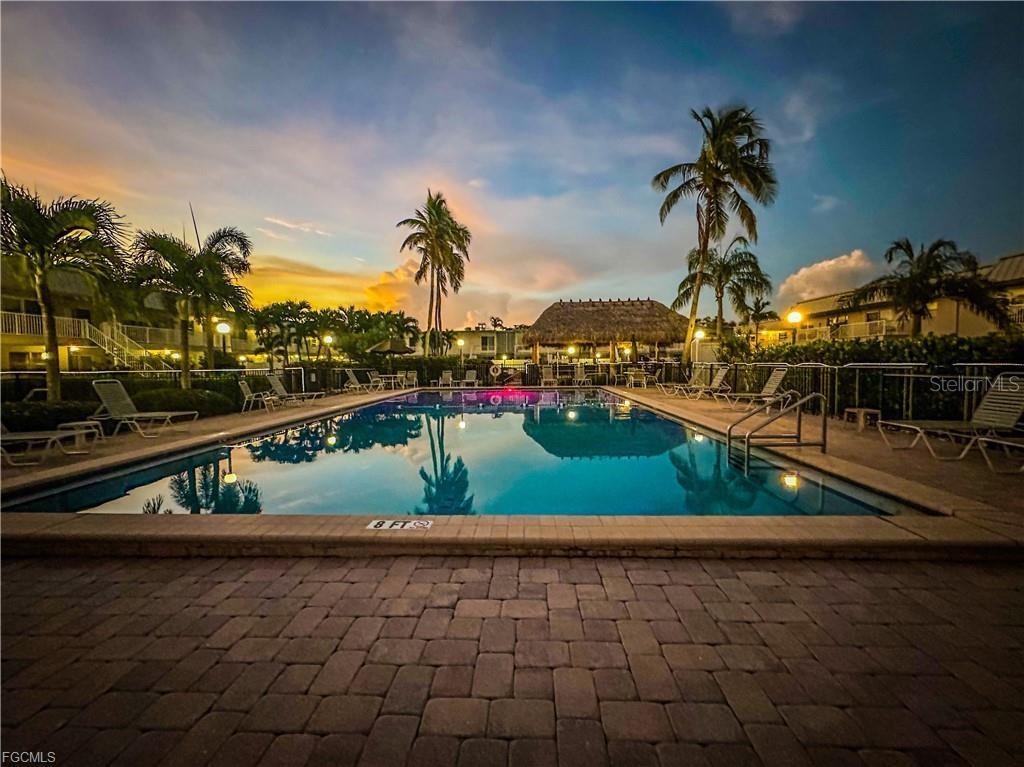A rectangular swimming pool is surrounded by a paver deck, lounge chairs, and palm trees — 6777 WINKLER ROAD UNIT 134, FORT MYERS, FL