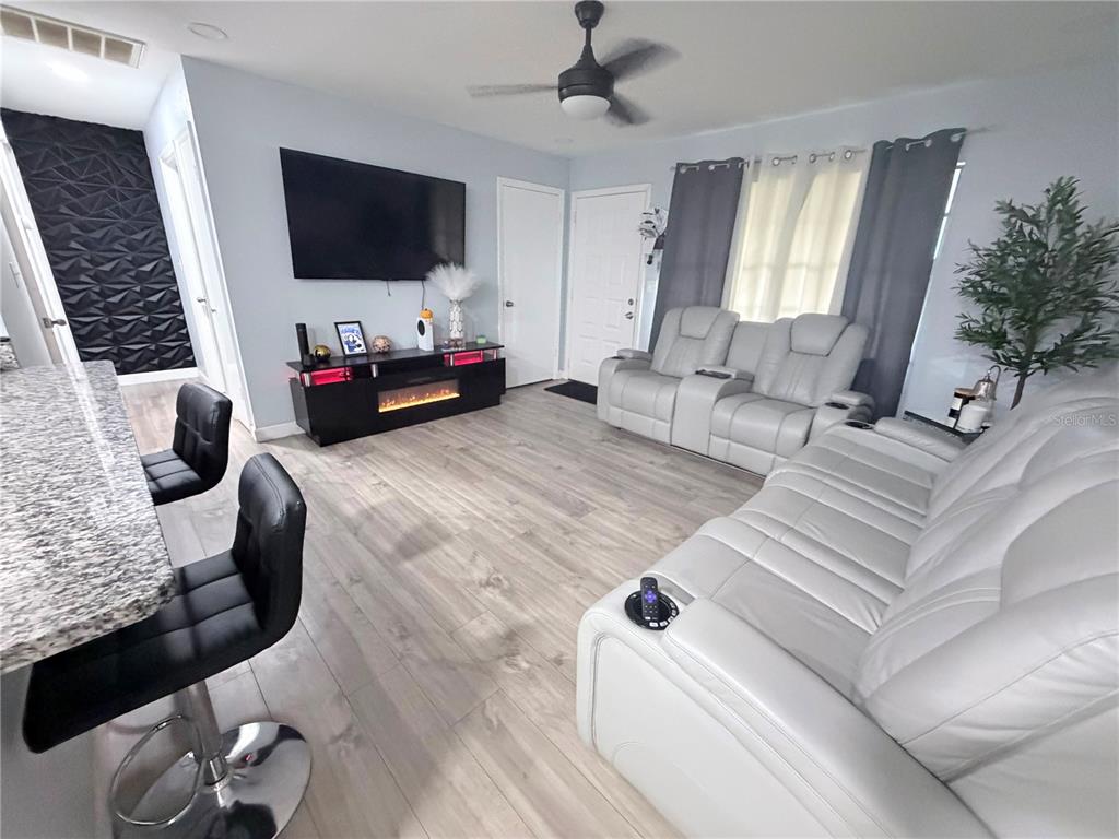 A living room features light wood flooring, a wall-mounted television, and white leather seating — 7281 SE 120TH STREET, BELLEVIEW, FL