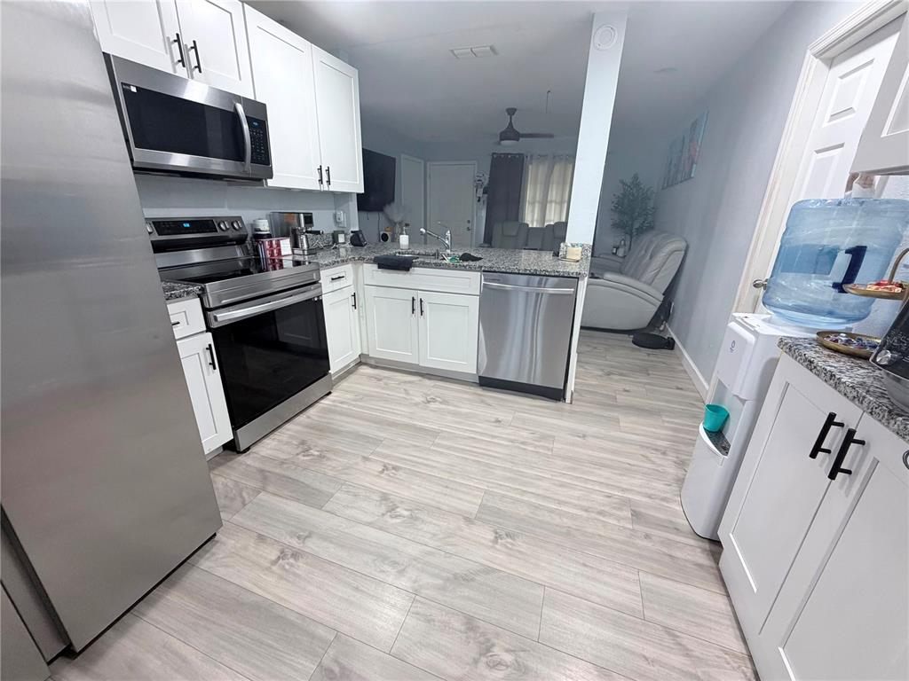 A kitchen features white cabinets, stainless steel appliances, granite countertops, and light wood-look flooring — 7281 SE 120TH STREET, BELLEVIEW, FL