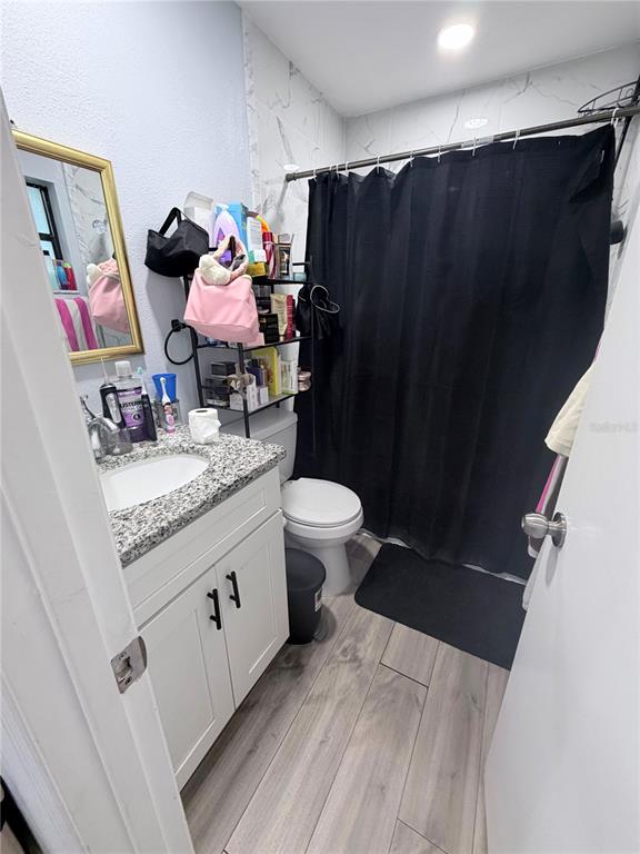 A bathroom features a vanity with a granite countertop, a toilet, and a black shower curtain — 7281 SE 120TH STREET, BELLEVIEW, FL