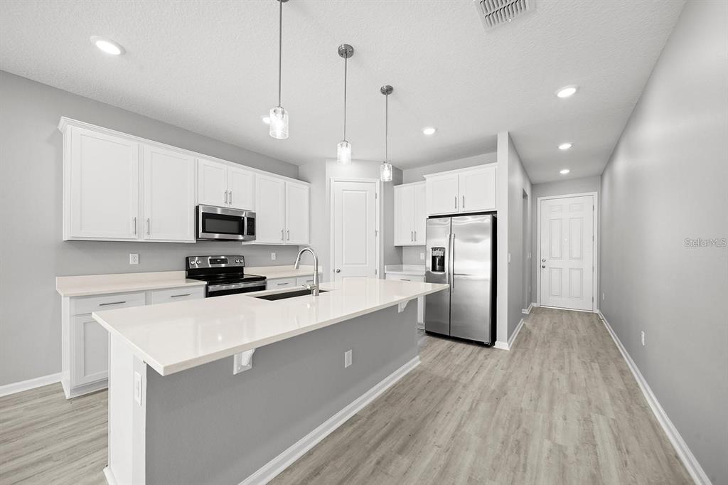 A modern kitchen features white cabinets, stainless steel appliances, a quartz island, and light flooring — 3003 FIN ROAD, WINTER HAVEN, FL