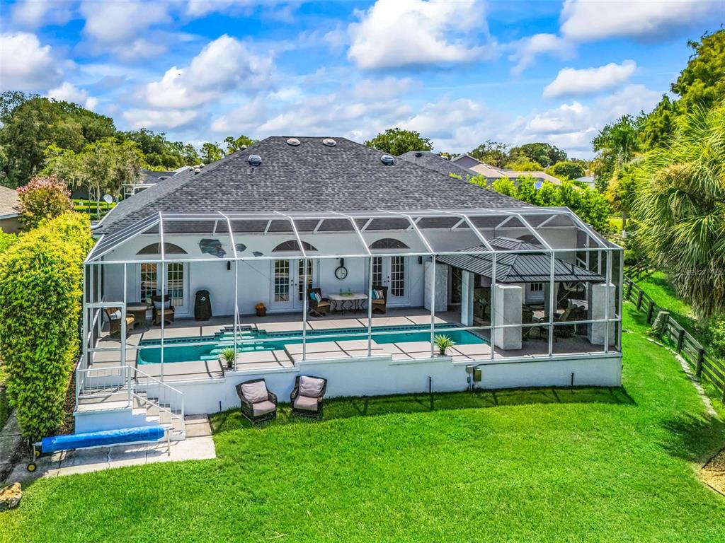 A backyard view of a house with a screened-in pool and a covered patio area — 714 CIMARRON AVENUE, THE VILLAGES, FL