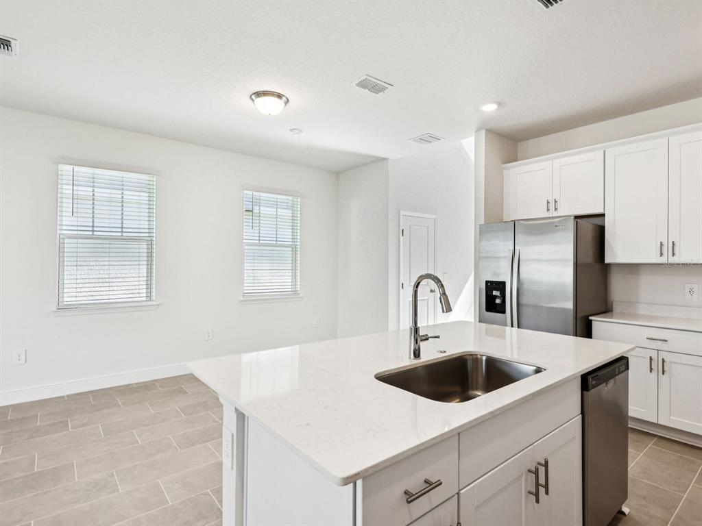 A kitchen features a white island with a sink, stainless steel appliances, and tile flooring — 2198 WILDBERRY WAY, MINNEOLA, FL