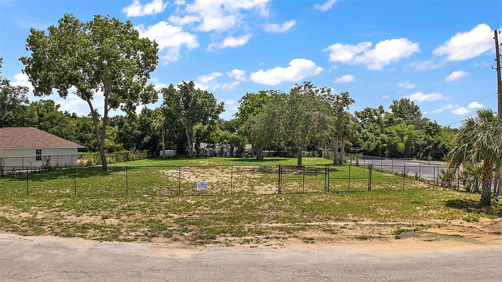 A fenced, vacant grassy lot with several mature trees sits next to a residential house — GORDON LANE, MOUNT DORA, FL