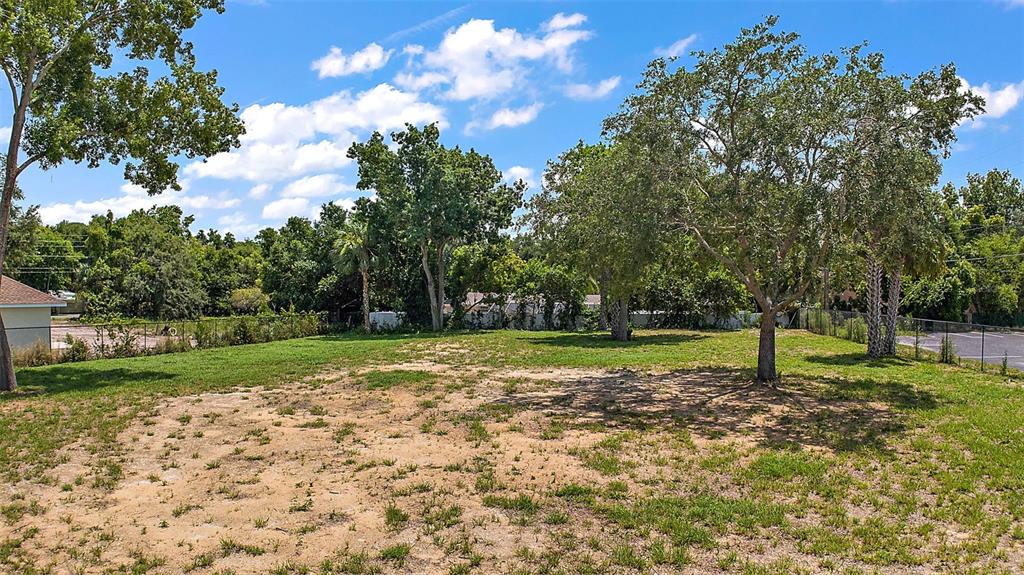 A grassy, partially cleared lot features several mature trees under a bright blue sky — GORDON LANE, MOUNT DORA, FL