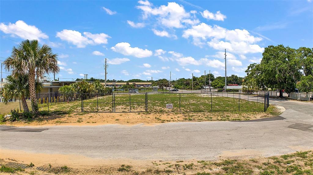 A fenced, vacant dirt lot sits beside a paved road with palm trees and greenery — GORDON LANE, MOUNT DORA, FL