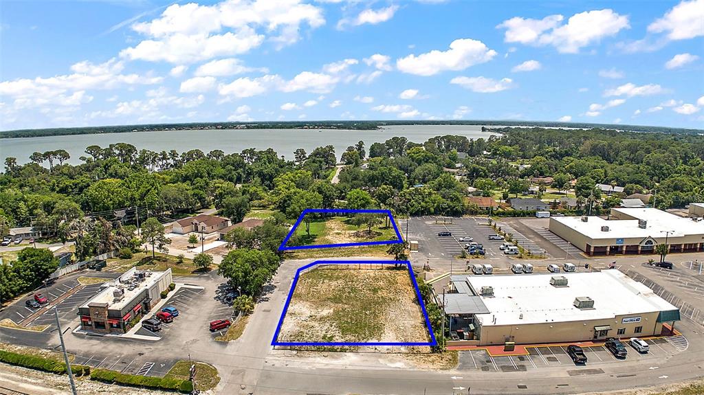 An aerial view shows two vacant, rectangular lots outlined in blue near commercial buildings and water — GORDON LANE, MOUNT DORA, FL