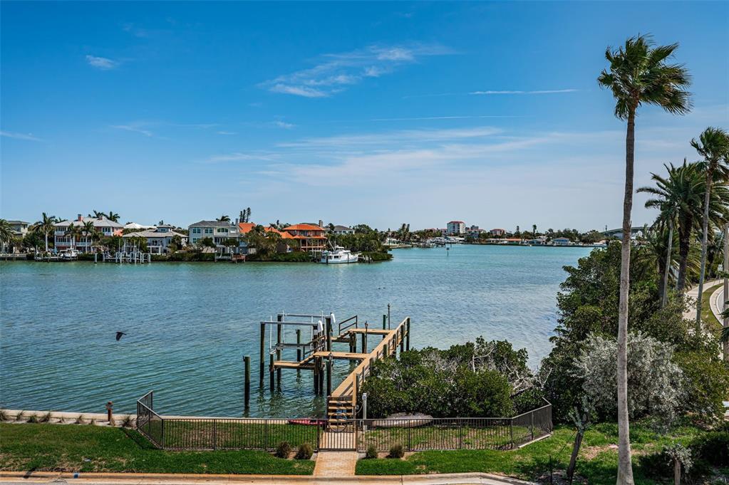 A wooden dock extends into a calm waterway surrounded by houses and palm trees — 3500 E MARITANA DRIVE UNIT 3, ST PETE BEACH, FL