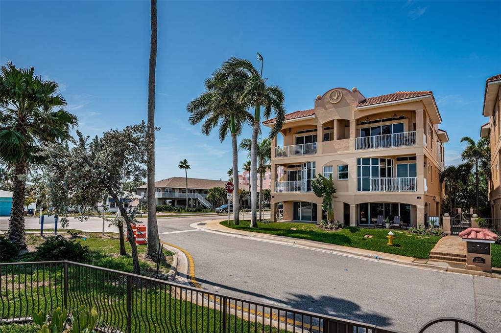 A three-story tan building with balconies stands near a street corner with palm trees — 3500 E MARITANA DRIVE UNIT 3, ST PETE BEACH, FL
