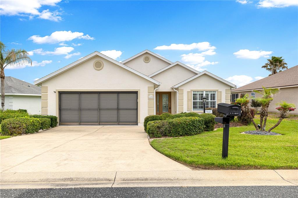 A single-story house with a beige stucco exterior, a two-car garage, and a front lawn — 11137 SE 173RD PLACE, SUMMERFIELD, FL