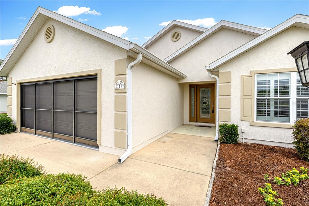 The exterior of a single-story house features a garage with a screen door and entryway — 11137 SE 173RD PLACE, SUMMERFIELD, FL