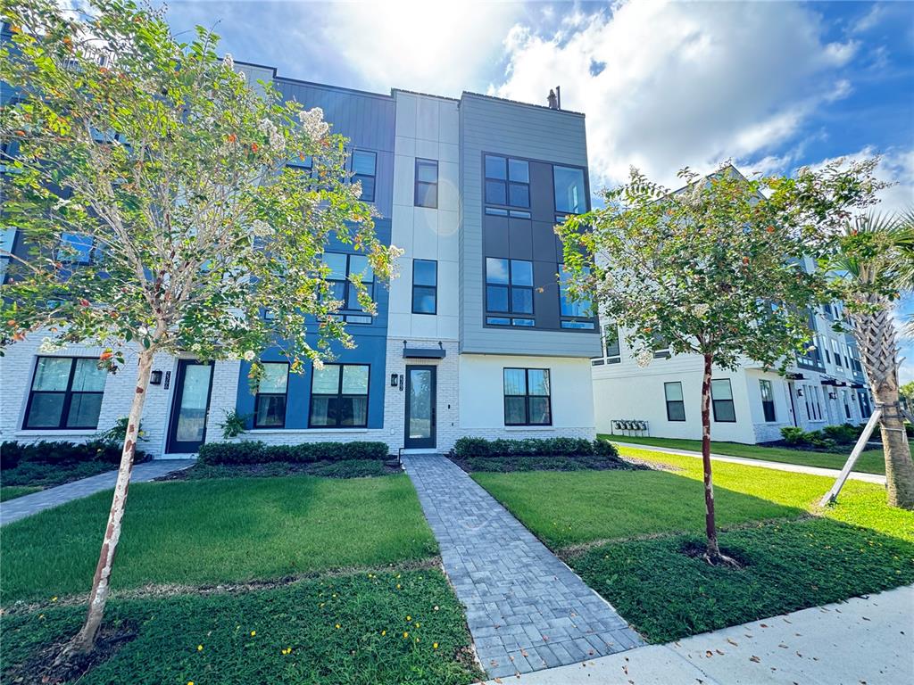 A three-story modern townhouse exterior features blue and white siding with a stone base — 2362 ADDALIA ALLEY, ORLANDO, FL
