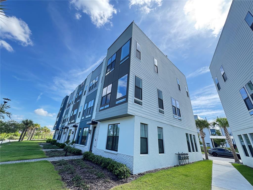 A low-angle exterior view of a modern three-story townhouse with light-colored siding and stucco — 2362 ADDALIA ALLEY, ORLANDO, FL