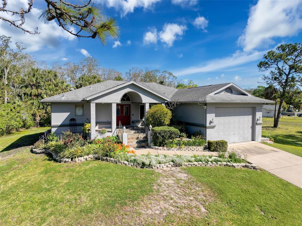 A single-story house with a gray exterior, a two-car garage, and a landscaped front yard — 8437 INDIES DRIVE, HUDSON, FL