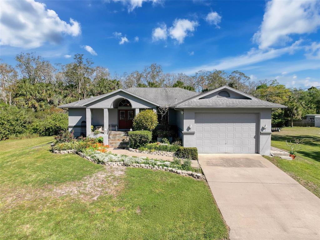 A single-story gray house with a two-car garage and a landscaped front yard — 8437 INDIES DRIVE, HUDSON, FL