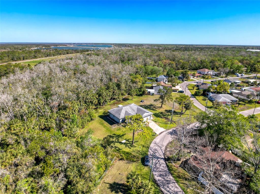 An aerial view shows a single-story house surrounded by trees and a nearby residential street — 8437 INDIES DRIVE, HUDSON, FL