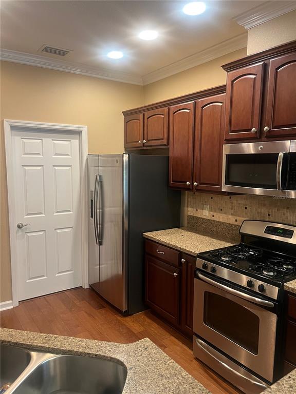 A kitchen features dark wood cabinets, stainless steel appliances, granite countertops, and hardwood flooring — 1385 ABBOT WAY, DELAND, FL