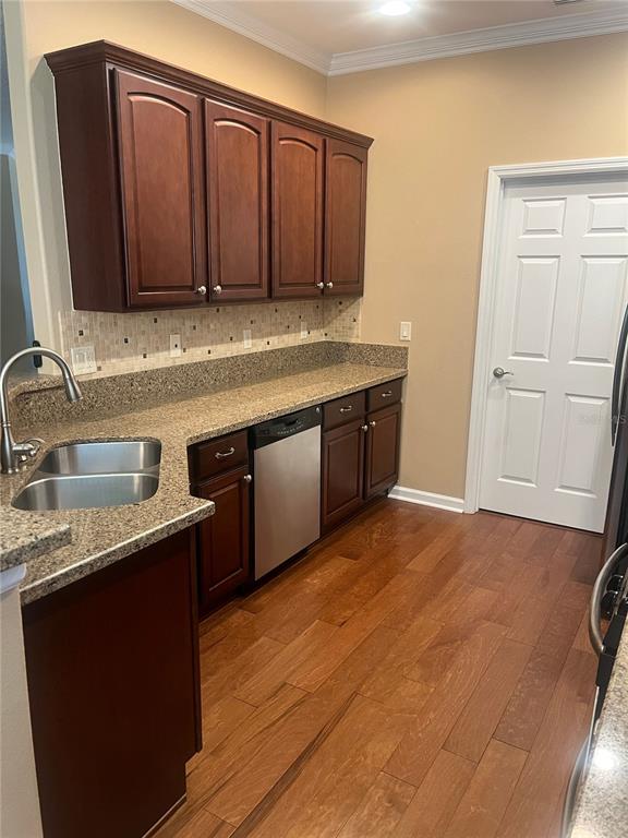 A kitchen features dark wood cabinets, granite countertops, a stainless steel dishwasher, and hardwood floors — 1385 ABBOT WAY, DELAND, FL