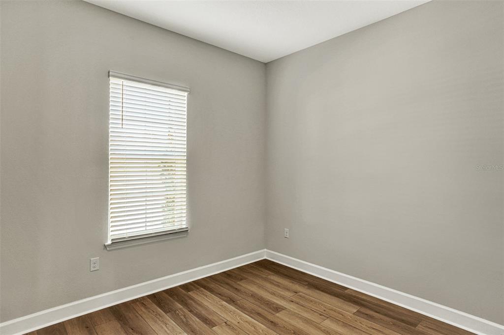 An empty room features light gray walls, white trim, and wood-look flooring with a window — 56 JACKSON BLUE DRIVE, PALM COAST, FL