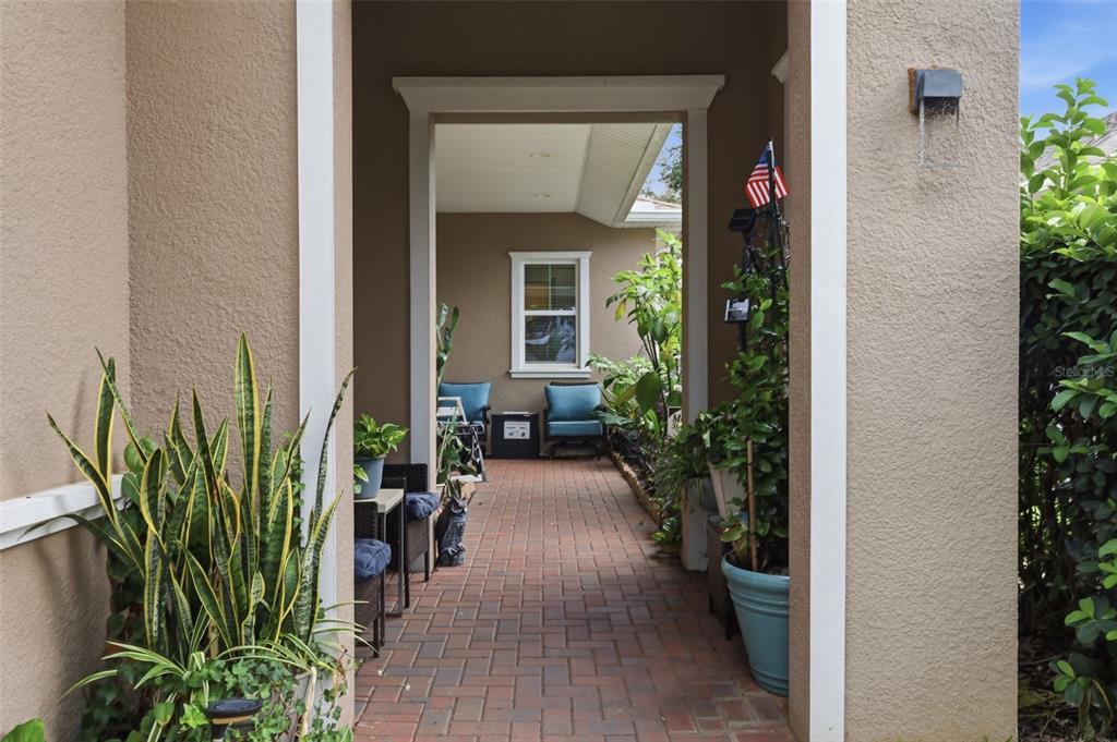 A covered brick patio features potted plants, two blue chairs, and a window — 273 SILVER MAPLE ROAD, GROVELAND, FL