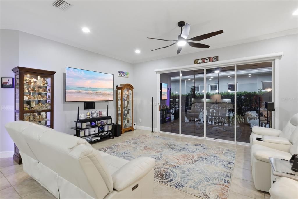 A living room features white leather sofas, a large television, display cabinets, and sliding glass doors — 273 SILVER MAPLE ROAD, GROVELAND, FL