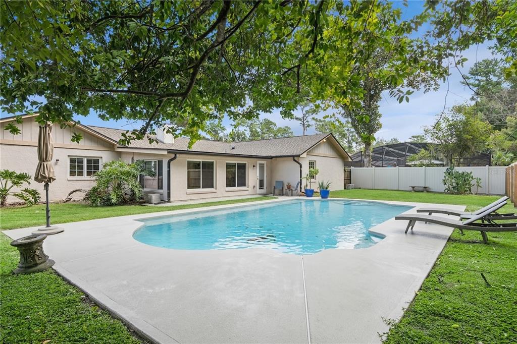 A backyard features a swimming pool, concrete patio, and a single-story house with light-colored siding — 734 RIVERBEND BOULEVARD, LONGWOOD, FL