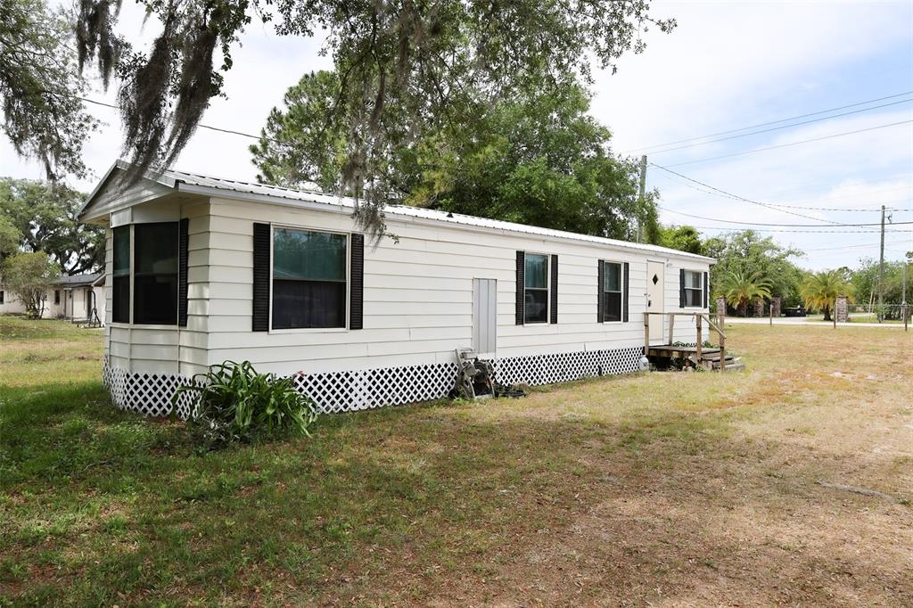 A white mobile home with black shutters sits on a grassy lot under trees — 220 KING ROAD, WINTER HAVEN, FL