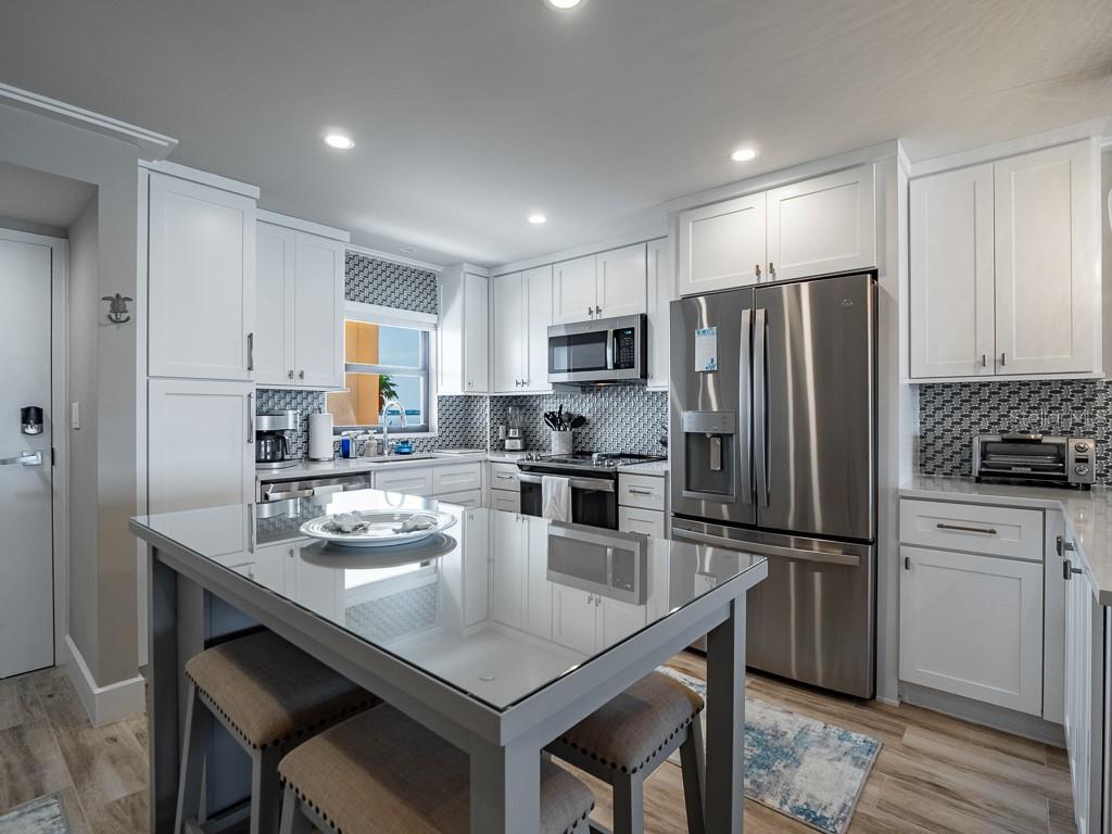 A modern kitchen features white cabinetry, stainless steel appliances, a glass-topped island, and patterned backsplash — 1270 GULF BOULEVARD UNIT 603, CLEARWATER, FL
