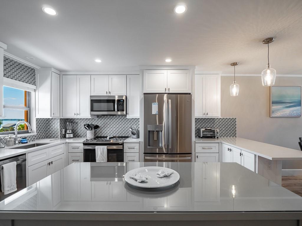 A modern kitchen features white cabinets, stainless steel appliances, a gray island, and patterned backsplash tile — 1270 GULF BOULEVARD UNIT 603, CLEARWATER, FL