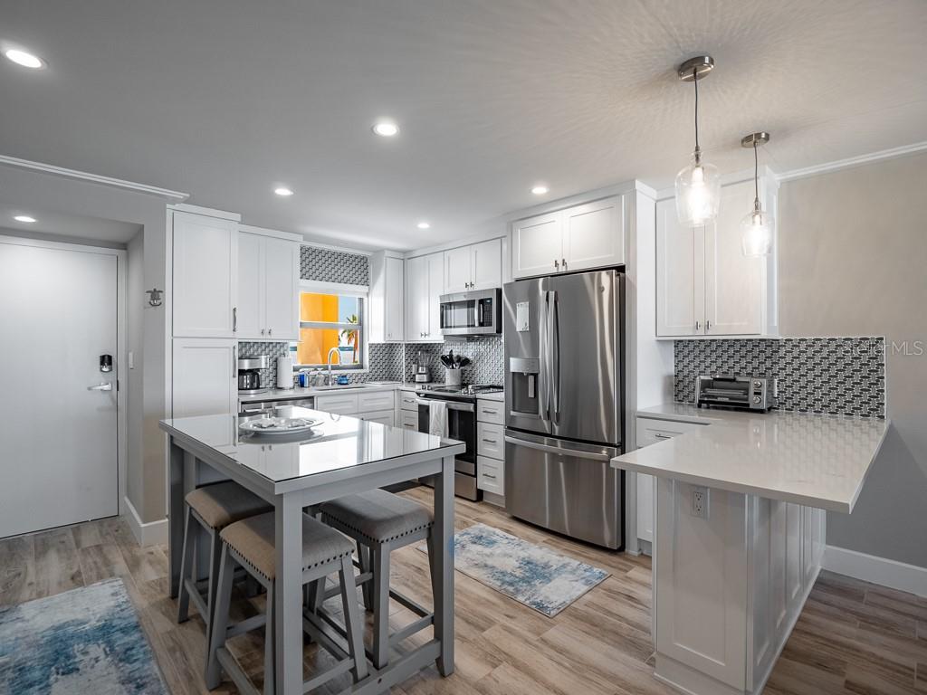 A modern kitchen features white cabinetry, stainless steel appliances, a glass-topped island, and patterned backsplash — 1270 GULF BOULEVARD UNIT 603, CLEARWATER, FL