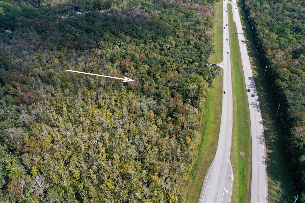 An aerial view shows a wooded lot adjacent to a divided highway with an arrow — W INDIAN RIVER BOULEVARD, EDGEWATER, FL