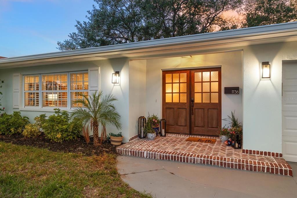 The exterior of a house features a brick porch, double wooden doors, and a window — 1736 GOLF VIEW DRIVE, BELLEAIR, FL