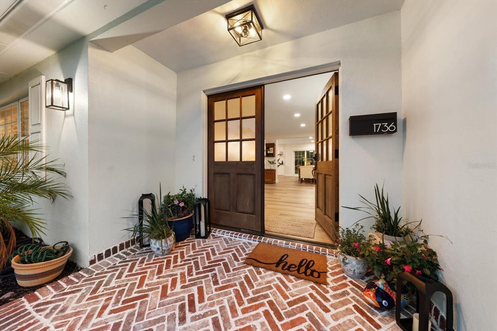 A front porch with a herringbone brick floor and a wooden door leading inside — 1736 GOLF VIEW DRIVE, BELLEAIR, FL