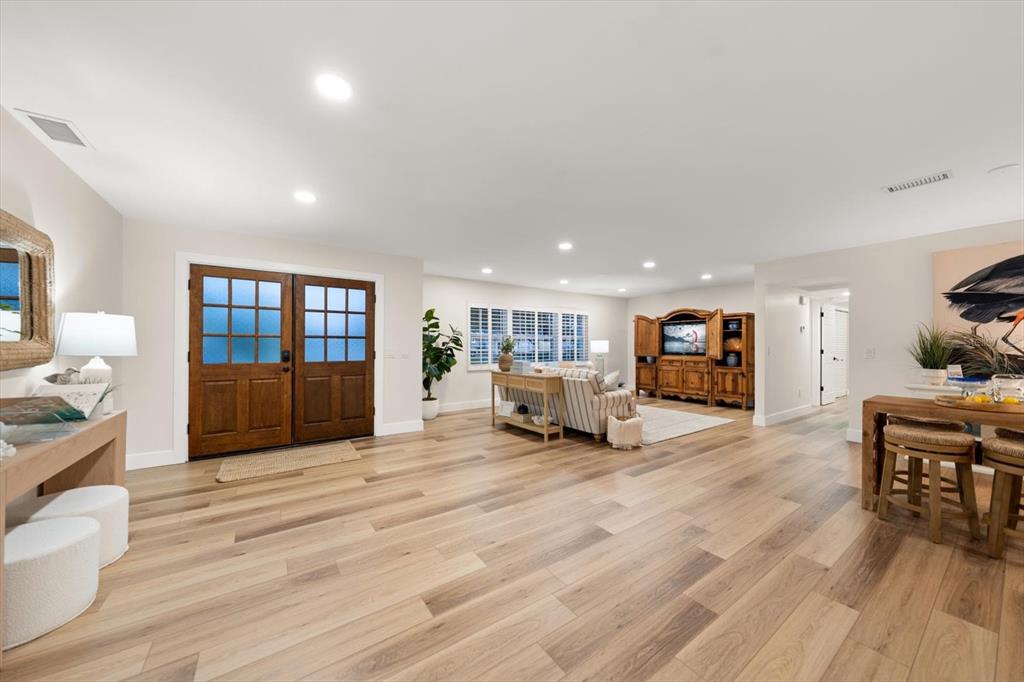 A spacious living room features light wood flooring, a double-door entryway, and a wooden entertainment center — 1736 GOLF VIEW DRIVE, BELLEAIR, FL