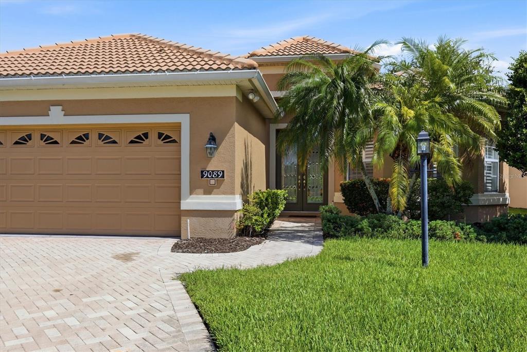A tan stucco house features a tile roof, a paved driveway, and a palm tree — 9089 WILLOW BROOK DRIVE, SARASOTA, FL